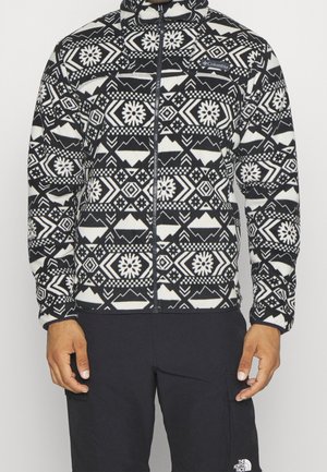Mężczyzna w czarno-białej wzorzystej polarowej kurtce Columbia z geometrycznymi i górskimi wzorami, w połączeniu z czarnymi spodniami The North Face.