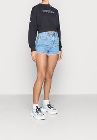 Černá zkrácená mikina s logem "LEVI'S", kombinovaná se světlými modrými džínovými kraťasy s třepenými lemy. Dokončeno robustními bílými teniskami.