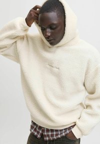 Crème fleece hoodie met een geprofileerd oppervlak, oversized pasvorm en een trekkoordcapuchon. Gelaagd over een geruit shirt, met ribgebreide manchetten.