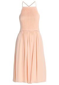 Robe sans manches en pêche avec un corsage plissé, une jupe froncée et de fines bretelles. Texture lisse avec des détails subtils le long de la couture.