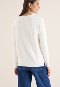 Witte, lange mouwen trui met een ronde hals; heeft een gestructureerde brei en zijsplitten. Gecombineerd met blauwe denim broek.