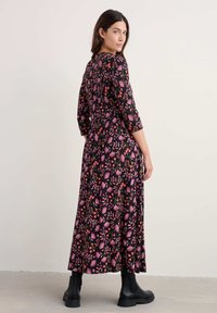 Cvećasta maksi haljina s crnom pozadinom, koja se ističe ružičastim i narančastim cvjetovima. Uređena s rukavima do tri četvrtine i uparena s crnim gležnjačama.