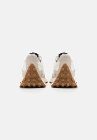 Light gray athletic shoes with a triangular tan rubber sole, suede accents, and a cushioned heel. White logo detail on the sides.