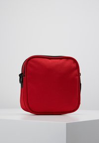 Red square-shaped bag made of textured fabric, featuring a black zip closure and a side handle for easy carrying.