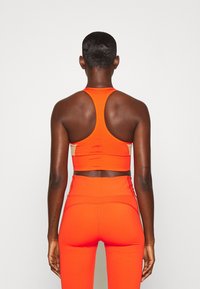 Orange atletisk crop top med racerback-design, kompletterad med matchande högmidjade leggings, båda i ett mjukt, elastiskt tyg.