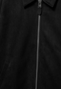 Schwarze Wildlederjacke mit silbernem Reißverschluss aus Metall und einem Kragen, zeigt Detail der vorderen Tasche auf der linken Seite.