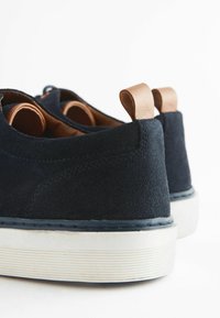 Tumesuede kingad valge tallaga, pruuni nahast detailide ja mugavaks kandmiseks kannas tõmbeotsa. Minimalistlik disain.