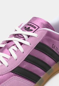 Pink ruskind sneakers med hvide snørebånd og tre sorte striber. Har et fremtrædende sort logo-patch på tungen. Gummisål.