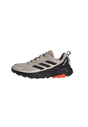 Chaussure d'extérieur beige avec une tige en maille, des accents noirs, une semelle texturée et des détails de talon orange vif. Conçue pour les terrains difficiles.