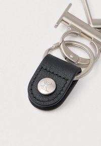 Sort lædernøglehænger med sølvmetalring og lukning, der har en rund sølvknap prægede med "cK" initialer.
