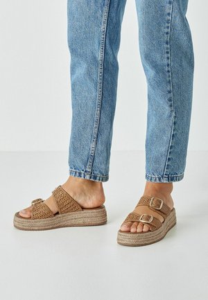 Sandales tressées marron avec deux brides à boucle réglables et une semelle plateforme enveloppée de jute. Portées avec un jean bleu à jambes droites.