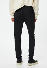 Pantalones de elasticidad negra con un corte ajustado, que cuentan con cinco bolsillos y una cinturilla texturizada. Combinados con zapatillas altas negras.