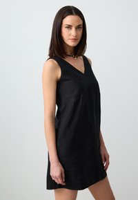 Schwarzes Leinenkleid mit V-Ausschnitt und ärmellosem Design. Besitzt eine lockere Silhouette und eine subtile Textur.