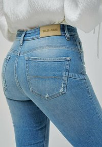Vaqueros de mezclilla azul con cintura alta, con una etiqueta de cuero "Salsa Jeans", bolsillos traseros y un ligero desgastado a lo largo de las costuras.