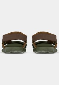 Πράσινα σανδάλια με υφασμένη σόλα από καουτσούκ, καφέ ιμάντες από νάιλον και ρυθμιζόμενες λεπτομέρειες στη φτέρνα. Η πίσω όψη αναδεικνύει το διπλό σχέδιο ιμάντα.