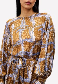 Braun gemustertes Kleid mit blauen Blumen- und Tiermotiven, langen Ärmeln und einem Taillenbindeband, aus einem leichten Stoff gefertigt.