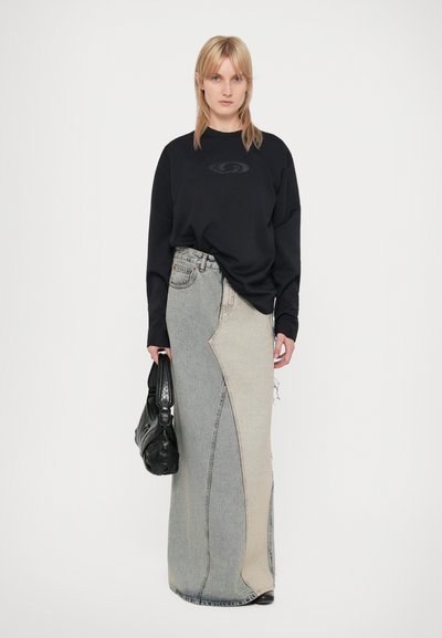 Zwarte sweatshirt met lange mouwen gecombineerd met een asymmetrische denimrok in lichte en donkere tinten, met gestructureerde zakken en een zwarte handtas.