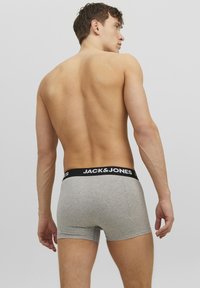 Graue Baumwoll-Boxershorts mit einem schwarzen elastischen Bund, der mit dem Logo "JACK & JONES" versehen ist. Das Modell wird von hinten gezeigt.