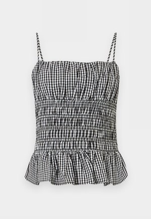 Svart-hvitt gingham smocket kamisolletopp med tynne stropper og en rysjekant mot en ensfarget bakgrunn.