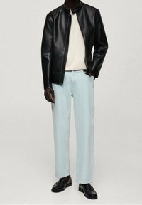 Czarna kurtka ze sztucznej skóry zapinana na zamek, na kremowym swetrze, w połączeniu z jasnoniebieskimi spodniami o prostych nogawkach oraz czarnymi skórzanymi butami.