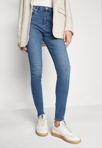 Trånga blå denimjeans med subtila blekningar, kombinerade med vita sneakers med en texturerad sula och svarta detaljer.