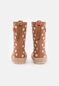Bottes de pluie en caoutchouc marron avec des motifs de cœurs blancs, dotées d'une sangle arrière et d'un logo sur le côté, semelle texturée pour une meilleure adhérence.
