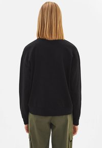 Felpa nera con una vestibilità rilassata, realizzata in tessuto morbido, con maniche lunghe e scollatura rotonda, abbinata a pantaloni cargo color oliva.