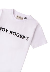Biała bawełniana koszulka z okrągłym dekoltem i krótkimi rękawami, z napisem "ROY ROGER'S" w pogrubionej czarnej czcionce na przedzie.