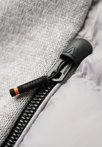 Tissu texturé gris avec une fermeture éclair noire ornée d'un accent orange. La tirette de la fermeture éclair est noire avec le texte "SUPERDRY" en relief.