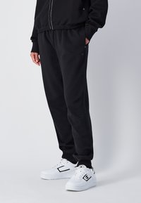 Zwarte joggingsbroeken van zachte stof met een elastische tailleband, zijzakken en een Champion-logo. Gekoppeld met witte sneakers.