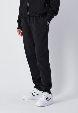 Schwarze Jogginghose aus weichem Material mit einem elastischen Bund, Seitentaschen und einem Champion-Logo. Kombiniert mit weißen Sneakers.