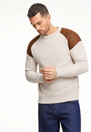 Beige ribbeltrui met bruine suède schouderpanelen. Ronde halslijn, lange mouwen en een aansluitende tailleband. Middelmatige dikte, textuurstof.