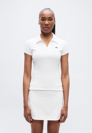 Biely športový polo set s sukňou vyrobený z hladkej, priliehavej látky, s krátkymi rukávmi a jemnou textúrou, s malým čiernym logom.
