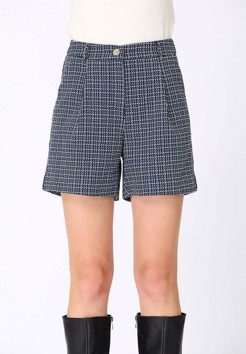 Shorts à taille haute à carreaux navy et blanc avec des plis, finis par un bouton à l'avant, associés à des bottes noires montantes.