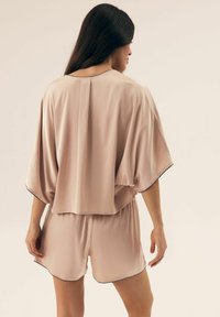 Jasnoróżowa satynowa bluzka z rękawami nietoperzami i czarnymi wykończeniami, w zestawie z dopasowanymi szortami. Tkanina ma gładką, błyszczącą teksturę.