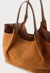 Hnědá semišová taška přes rameno s měkkou texturou, dvěma pevnými úchyty a zapínáním na druk. Vyznačuje se minimalistickým designem s hladkým vnitřním podšívkou.