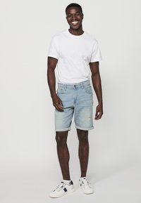 Shorts en denim bleu clair avec ourlets retroussés et détails déchirés, associés à un t-shirt blanc uni et des baskets blanches avec des accents navy.