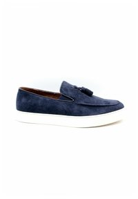 Chaussure slip-on en daim bleu marine avec un bout arrondi, un pompon décoratif et une semelle en caoutchouc blanche. Le design présente des lignes épurées et des accents minimalistes.