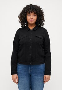 Black denim jacket with long sleeves, front button closure, two chest pockets, and a cropped design. Worn with blue jeans.