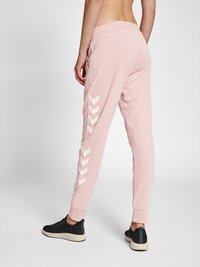 Rosa taperte Jogginghosen aus weichem Stoff, mit weißen Chevron-Akzenten an der Seite und elastischen Bündchen. Getragen mit schwarzern Sneakers.