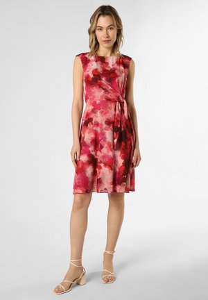 Blumenkleid in Rosa- und Rottönen, ärmellos mit einem Bindeband in der Taille. Leichte Stoffqualität, knielang, kombiniert mit beigen High-Heelsandalen.