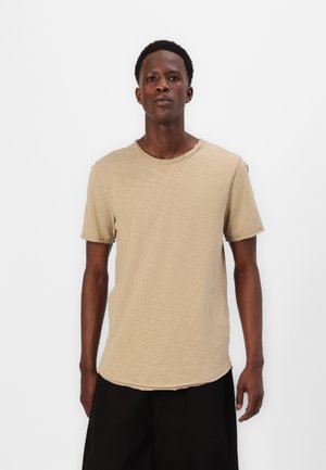 Hellbeige T-Shirt mit kurzen Ärmeln und rundem Ausschnitt, weicher Textur, lockerer Passform und rohem Saum, kombiniert mit weit geschnittenen schwarzen Shorts.