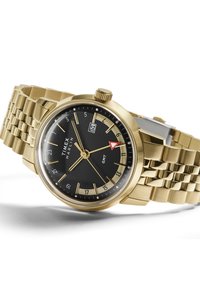 Arany tónusú Timex Marlin óra fekete számlappal, rozsdamentes acél karkötővel, kerek tokban, GMT funkcióval és 3 óránál dátum kijelzővel.