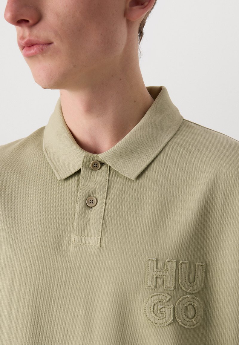 Polo shirt vert clair en coton texturé. Doté d'un col classique, d'une patte de boutonnage à trois boutons et d'un logo "HUGO" brodé sur la poitrine.