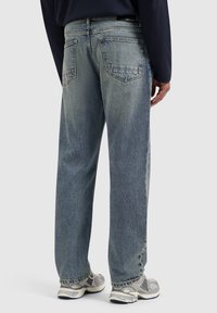 Lichtblauwe denim jeans met een relaxed fit, voorzien van achterzakken en een vervaagde textuur, gecombineerd met grijze sneakers.