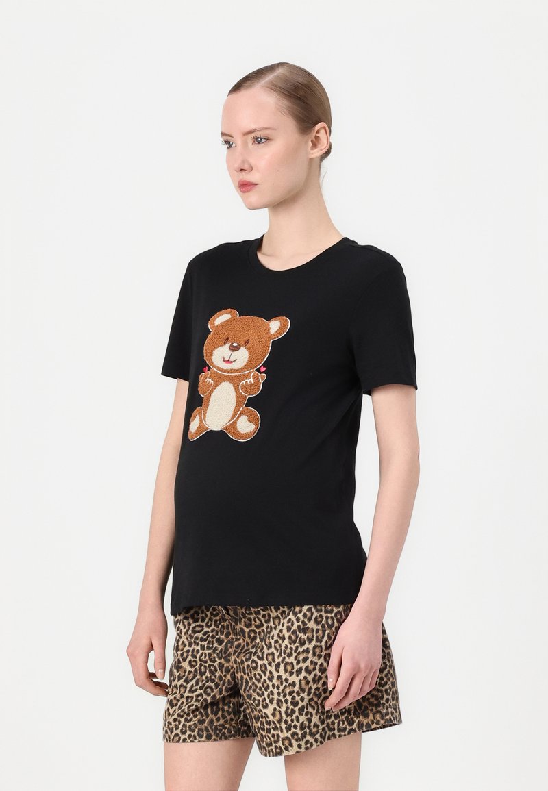 Melna T-kreklu ar brūnu lāču grafiku, ar gaišākām akcentiem un smaidīgu izteiksmi. Saskaņota ar leoparda raksta šortiem.