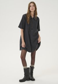 Mörk jeansskjortklänning med dragkedja fram, korta ärmar och sidslitsar. Bärs tillsammans med svarta läderstövlar som går upp till knäna och knä-långa strumpor.