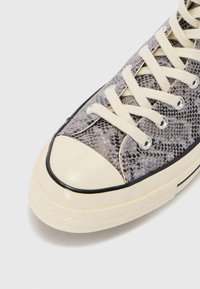 Sneaker with a textured snake print upper in shades of gray, cream rubber toe cap, black trim, and cream laces.