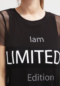 Svart nät t-shirt med djärv text: "Jag är en BEGRÄNSAD upplaga" i vitt. Mjuk tyg med avslappnad passform och genomskinliga ärmar.