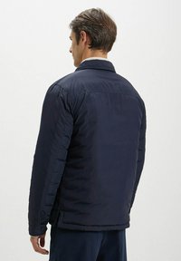 Giacca blu navy con texture trapuntata, dotata di colletto, polsini con bottone e taglio dritto, mostrata da dietro.